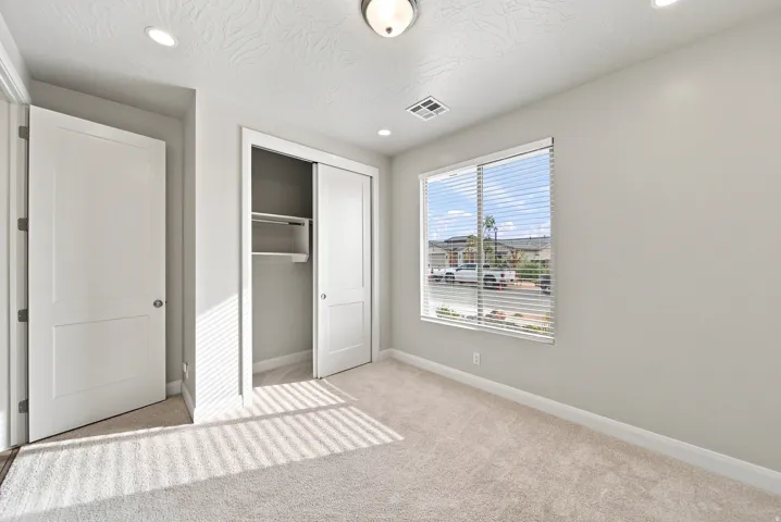 Neutral wall paint, carpeted flooring, window with blinds, recessed lighting, and a closet with sliding doors