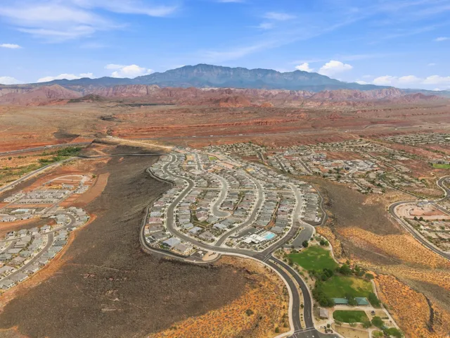 Expansive residential development with a mountain backdrop, featuring a large community pool, manicured green spaces, and paved roadways