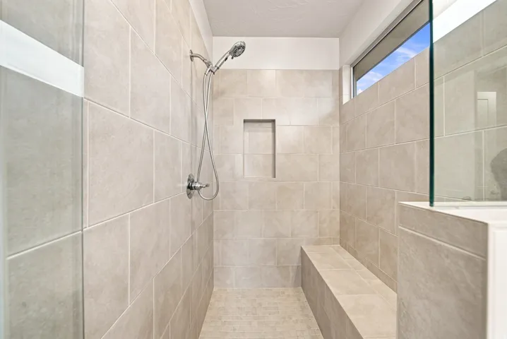 Tiled shower enclosure with a built-in bench, recessed niche, transom window, and a glass partition