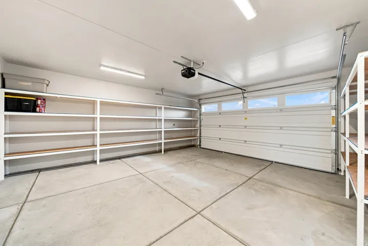 Attached garage with a concrete floor, built-in shelving, overhead lighting, and an automatic garage door opener