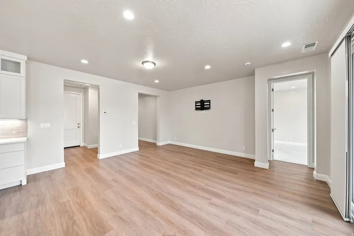 Recessed lighting, wood-finish flooring, white cabinetry, light-toned walls, and a sliding glass door