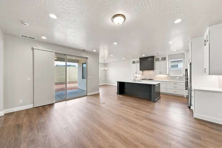 Wood-finish flooring, recessed lighting, sliding glass door, white cabinetry, and a dark kitchen island with a light countertop