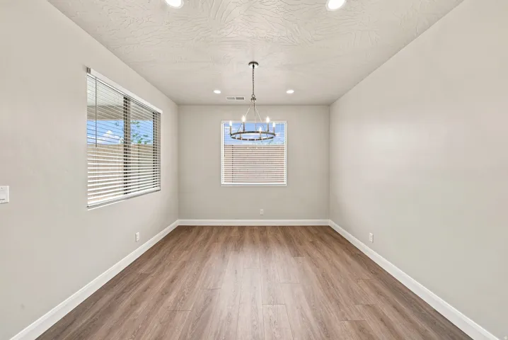 Recessed lighting, wood-finish flooring, two windows with blinds, and a contemporary chandelier