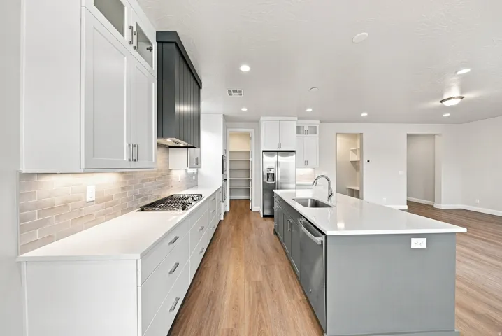 Kitchen featuring an expansive island with a stainless steel sink, wood-finish flooring, white cabinetry, a tiled backsplash, and stainless steel appliances