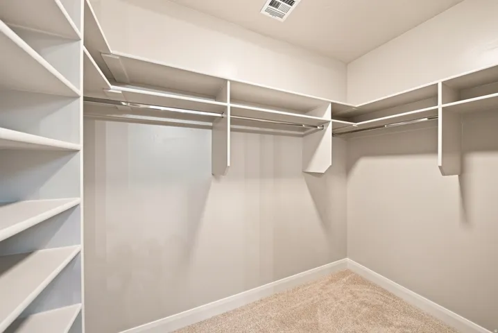 Walk-in closet featuring extensive built-in shelving, multiple hanging rods, and neutral-toned carpeting