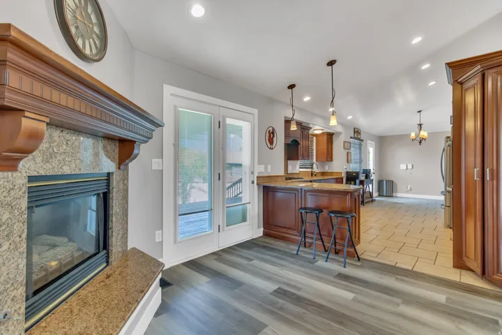 Granite fireplace surround with wood mantel, double French doors, wood-finish flooring, kitchen island with seating, and stainless steel refrigerator