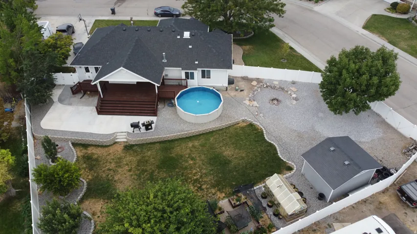 Expansive backyard featuring a covered wood deck, concrete patio, above-ground pool, and a gravel fire pit area
