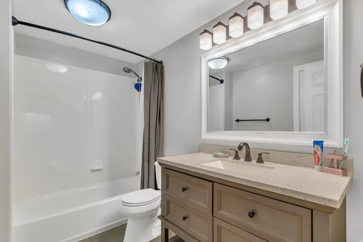 Bathroom featuring a built-in tub with shower, single vanity with a light-toned countertop, framed mirror, and a five-light fixture