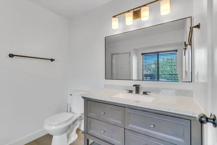 Gray vanity with integrated sink, speckled white countertop, and wall-mounted light fixture