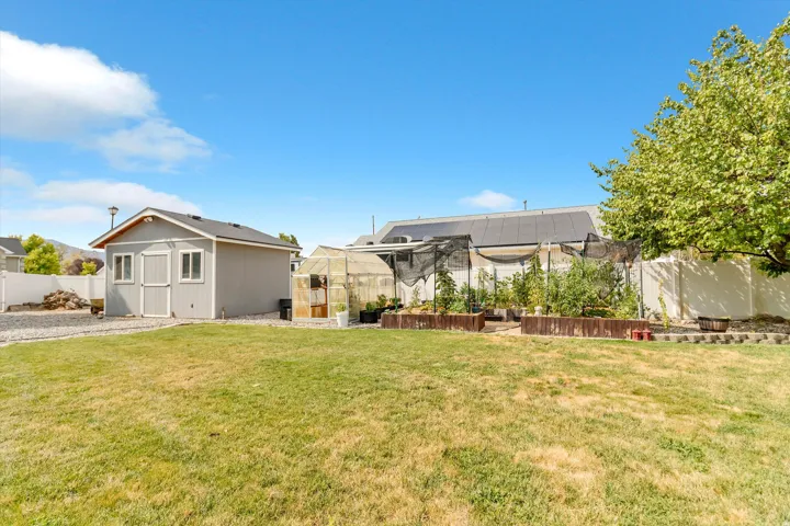 Expansive backyard featuring a dedicated storage shed, functional greenhouse, and raised garden beds
