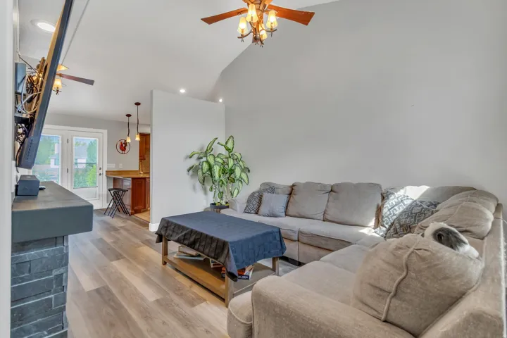 Living area with wood-finish flooring, vaulted ceiling, recessed lighting, and a stone-clad fireplace