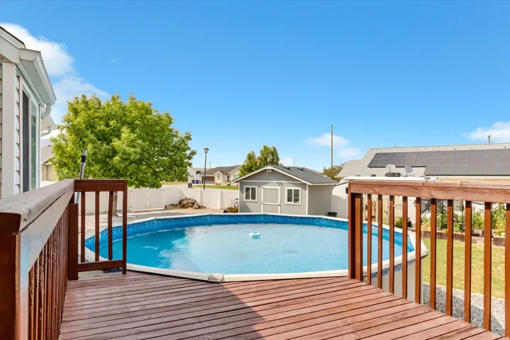 Wood-finish deck with railing overlooking an above-ground pool and a detached storage shed
