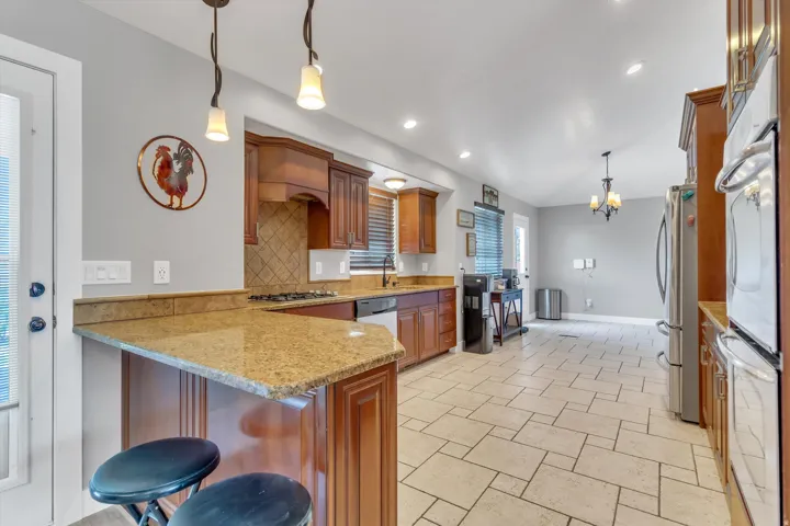 Kitchen featuring a breakfast bar with granite countertops, wood-finish cabinetry, stainless steel appliances, and tile flooring