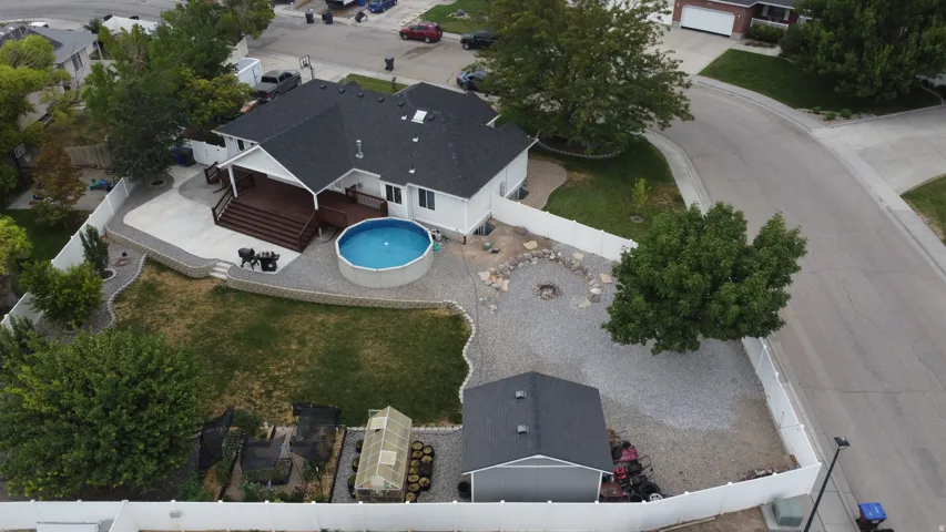 Expansive rear yard featuring a wood deck, concrete patio, above-ground swimming pool, and a gravel entertainment area with a fire pit