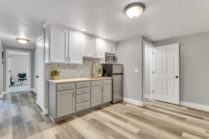 Compact kitchen with two-tone cabinetry, a mosaic tile backsplash, wood-finish flooring, recessed lighting, and a stainless steel appliance suite