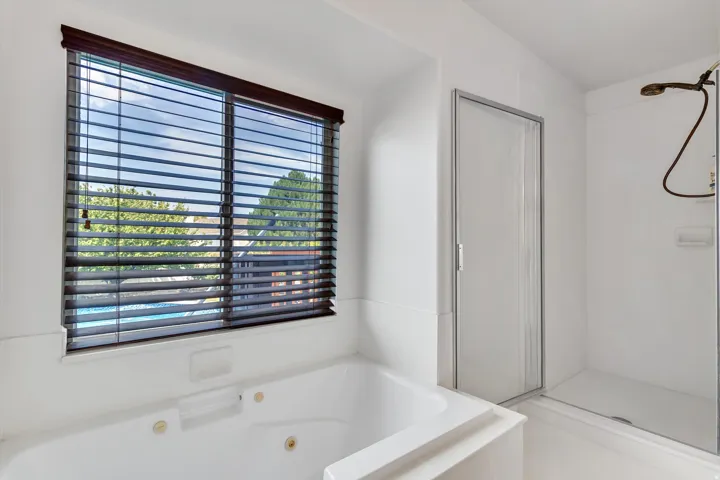 Soaking tub with integrated jets, wood-finish blinds, and an enclosed shower with a bronze-finish showerhead
