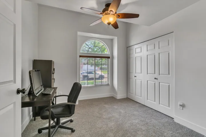 Arched window with blinds, ceiling fan with light fixture, and paneled closet doors