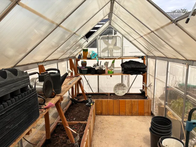 Greenhouse structure featuring translucent paneling, wood-frame shelving, and built-in wood-sided planters