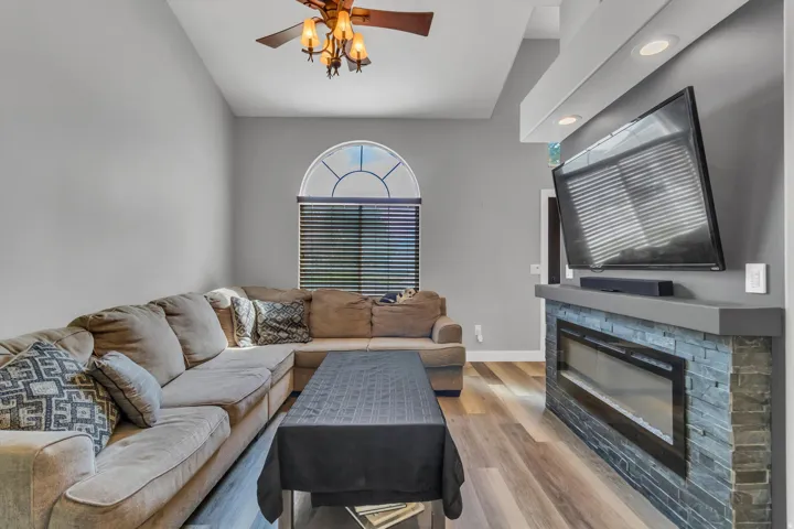 Vaulted ceiling with an attached ceiling fan, arched window, wood-finish flooring, and a stone-clad fireplace