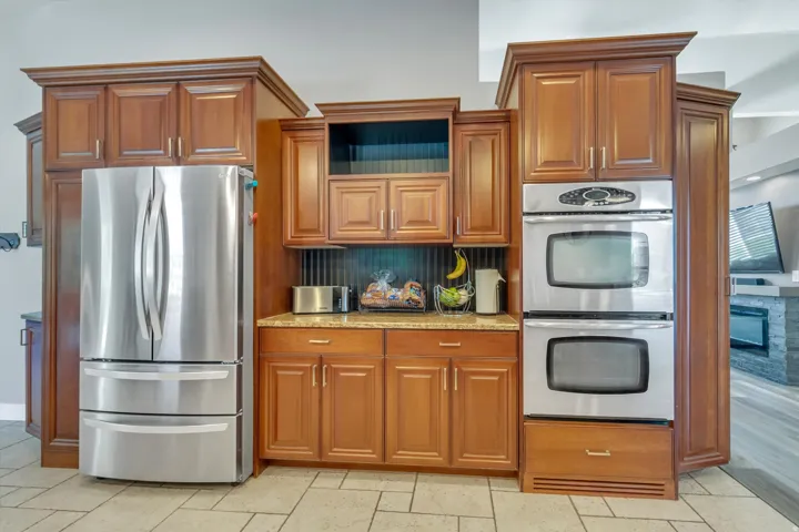 Wood cabinetry with crown molding, stainless steel French door refrigerator, light-toned countertop, and stainless steel double wall ovens