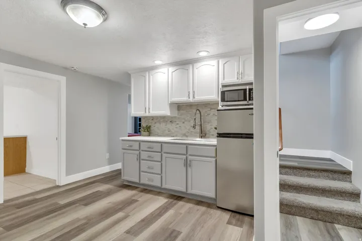 Kitchenette featuring white cabinetry, a stainless steel refrigerator, microwave, and a tile backsplash