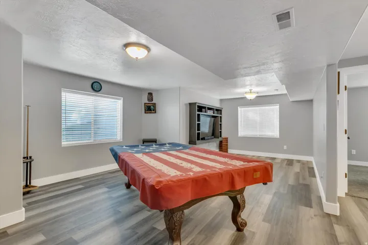 Spacious room featuring light gray walls, wood-finish flooring, two windows with blinds, and recessed lighting