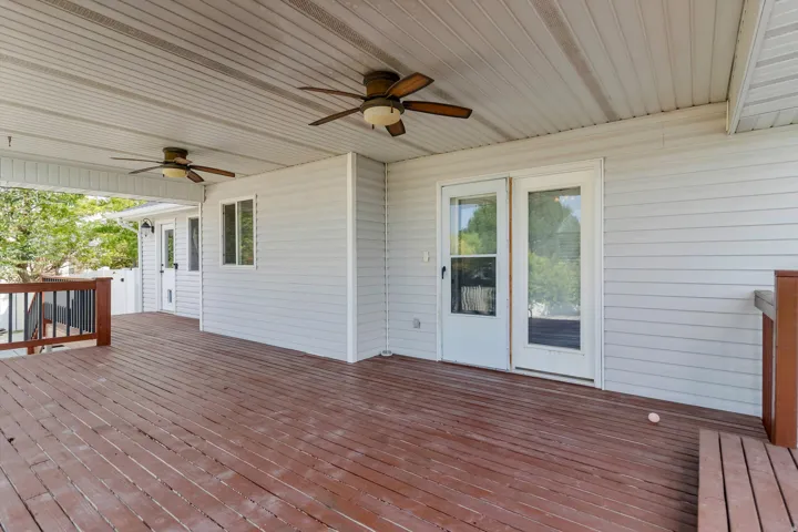 Expansive covered deck featuring wood decking, white vinyl siding, and two ceiling fans