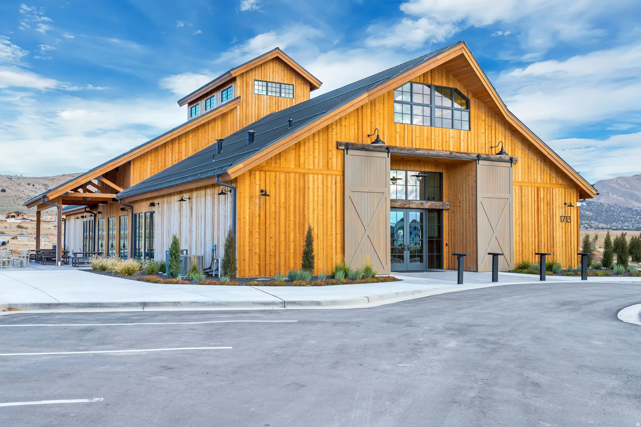 Barn-style architecture featuring natural wood siding, prominent sliding barn doors, a cupola, a metal roof, and large windows