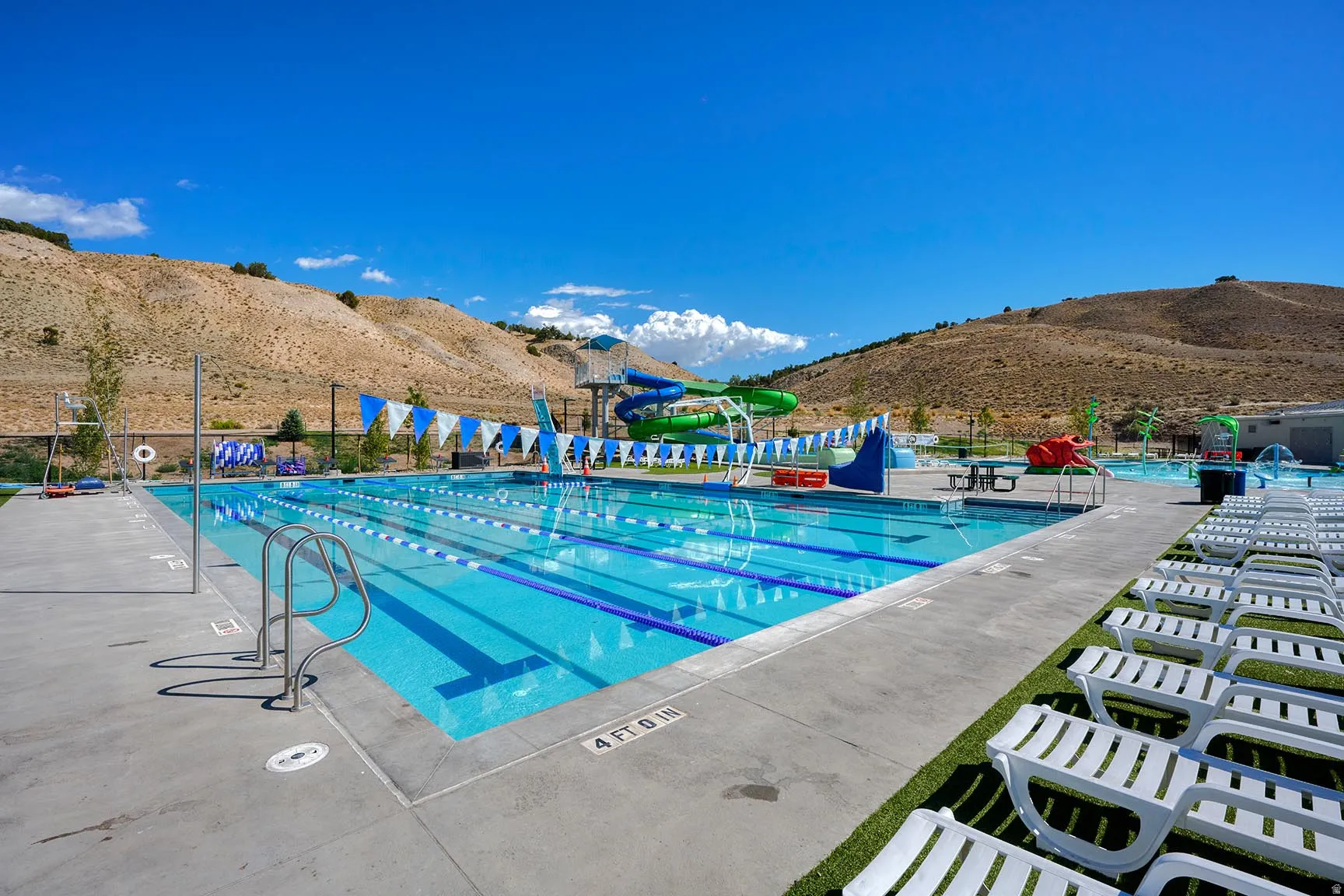 Community pool with multiple swimming lanes, concrete decking, water slides, and synthetic turf areas