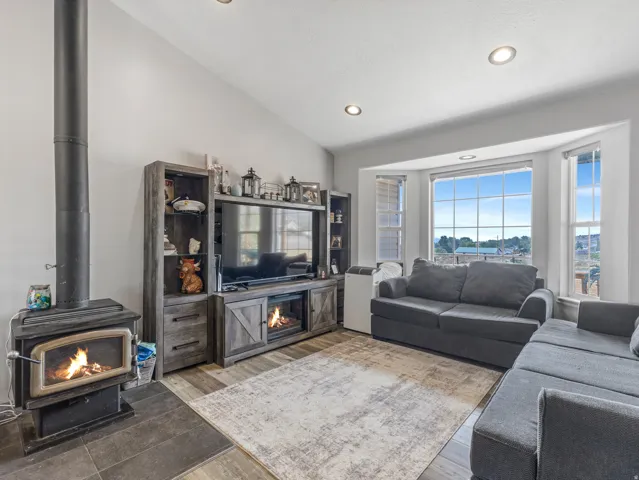 Modern living room anchored by a wood-finish entertainment center with integrated cabinetry and shelving, paired with a cast-iron wood-burning stove featuring a black metal surround