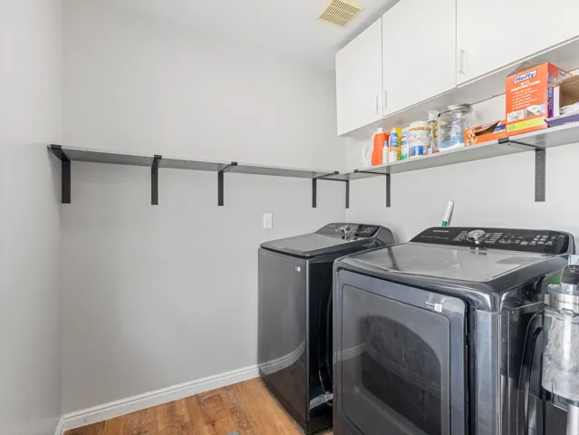 Wood-finish flooring with white baseboards, white upper cabinetry, and wall-mounted shelving