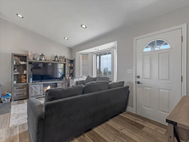 Vaulted ceiling with recessed lighting, wood-finish flooring, bay window, white paneled entry door with transom