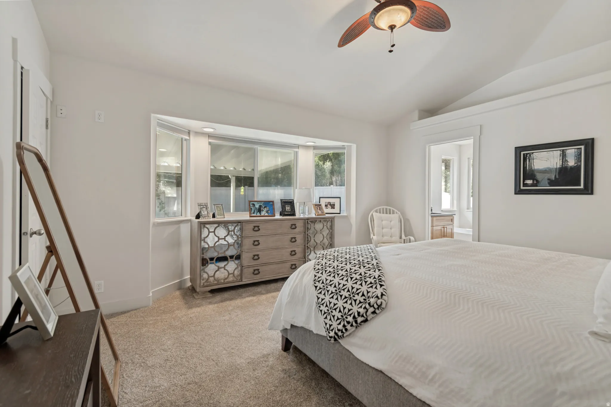 Bay window with sill, vaulted ceiling, ceiling fan, and carpeted flooring