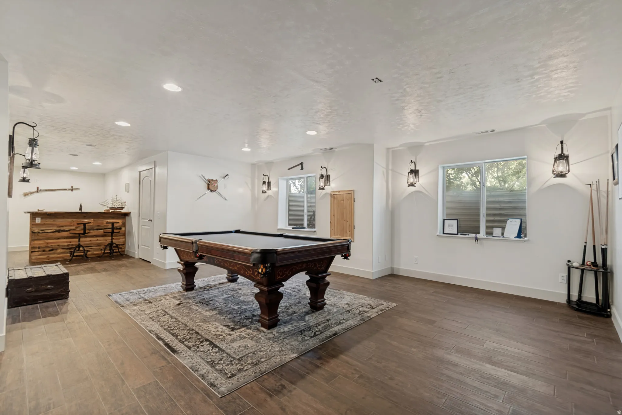 Spacious recreation room featuring rich wood-finish flooring throughout, a full-size pool table with professional-grade felt, recessed ceiling lighting, and pendant fixtures
