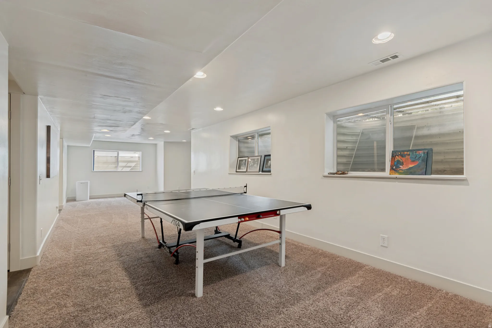 Expansive carpeted area with recessed lighting, multiple windows, and white painted walls