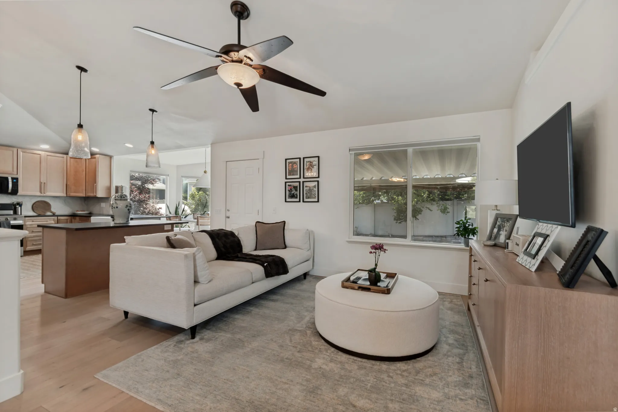 Open-concept living space featuring a cream upholstered sofa, wood-finish flooring throughout, and a ceiling fan with integrated lighting
