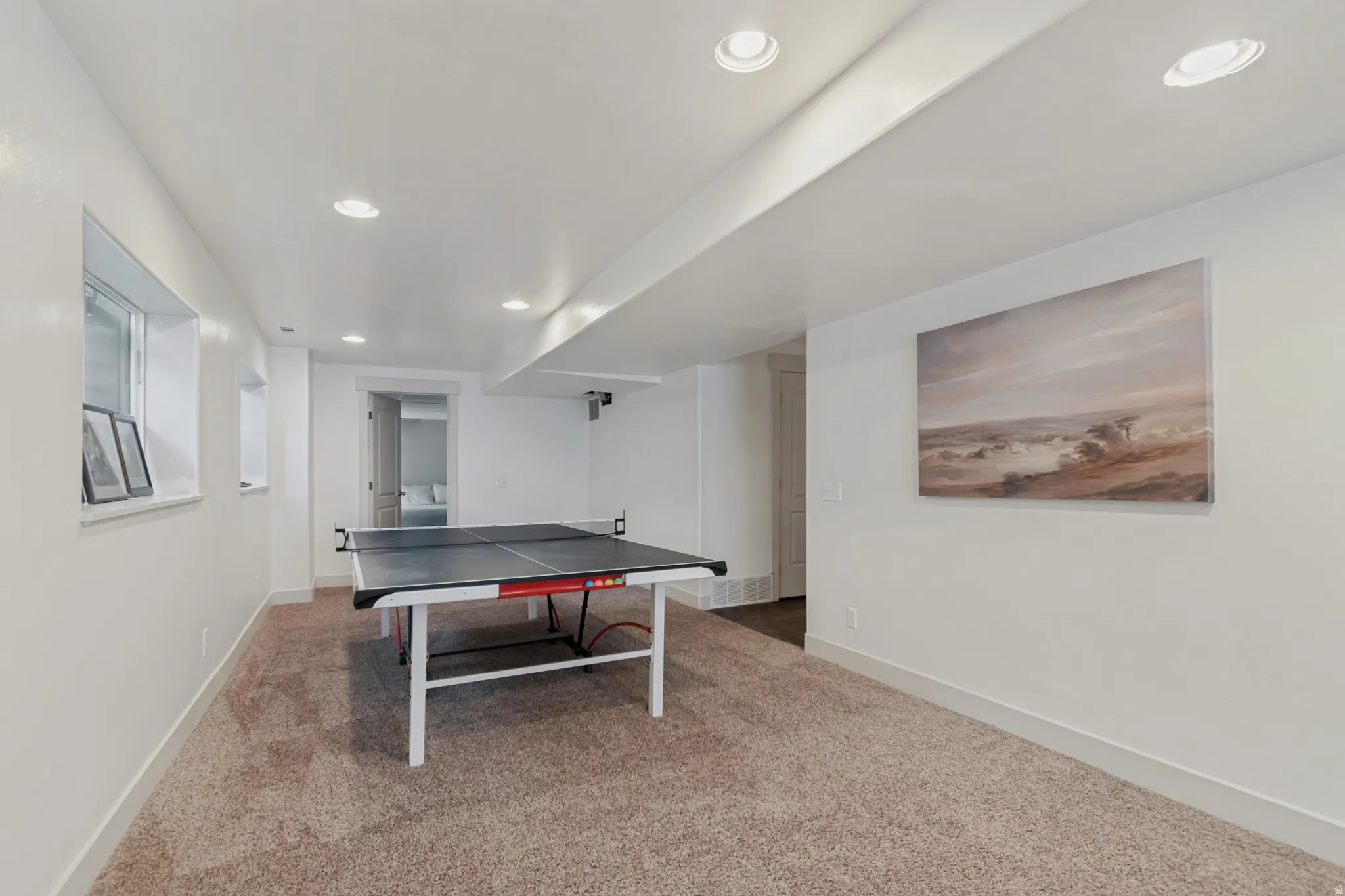 Finished recreation room featuring neutral carpet flooring, recessed lighting throughout the ceiling, and white walls with soft accent artwork