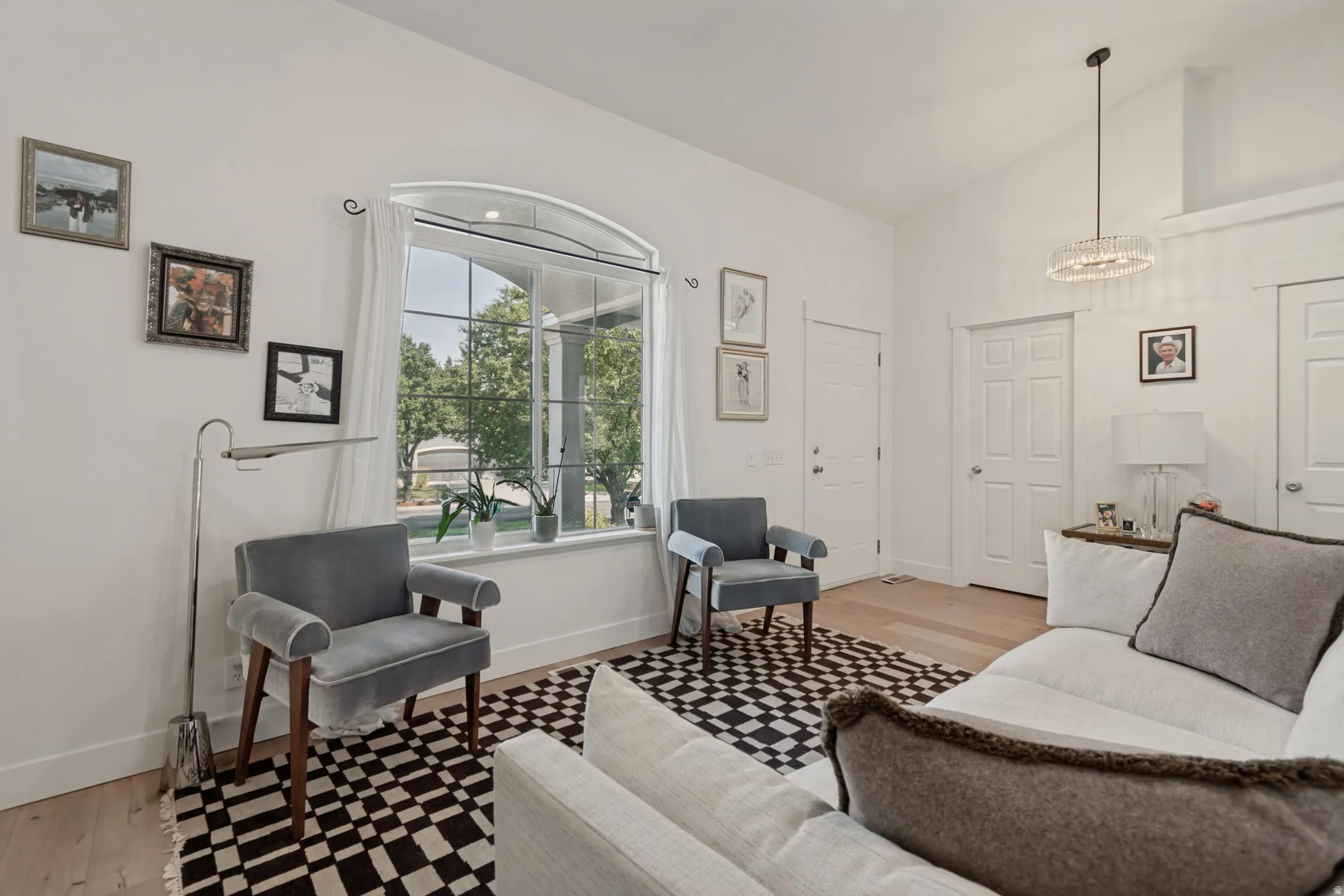 Bright bedroom featuring hardwood flooring, a large arched window with natural light, geometric patterned area rug, and white six-panel doors
