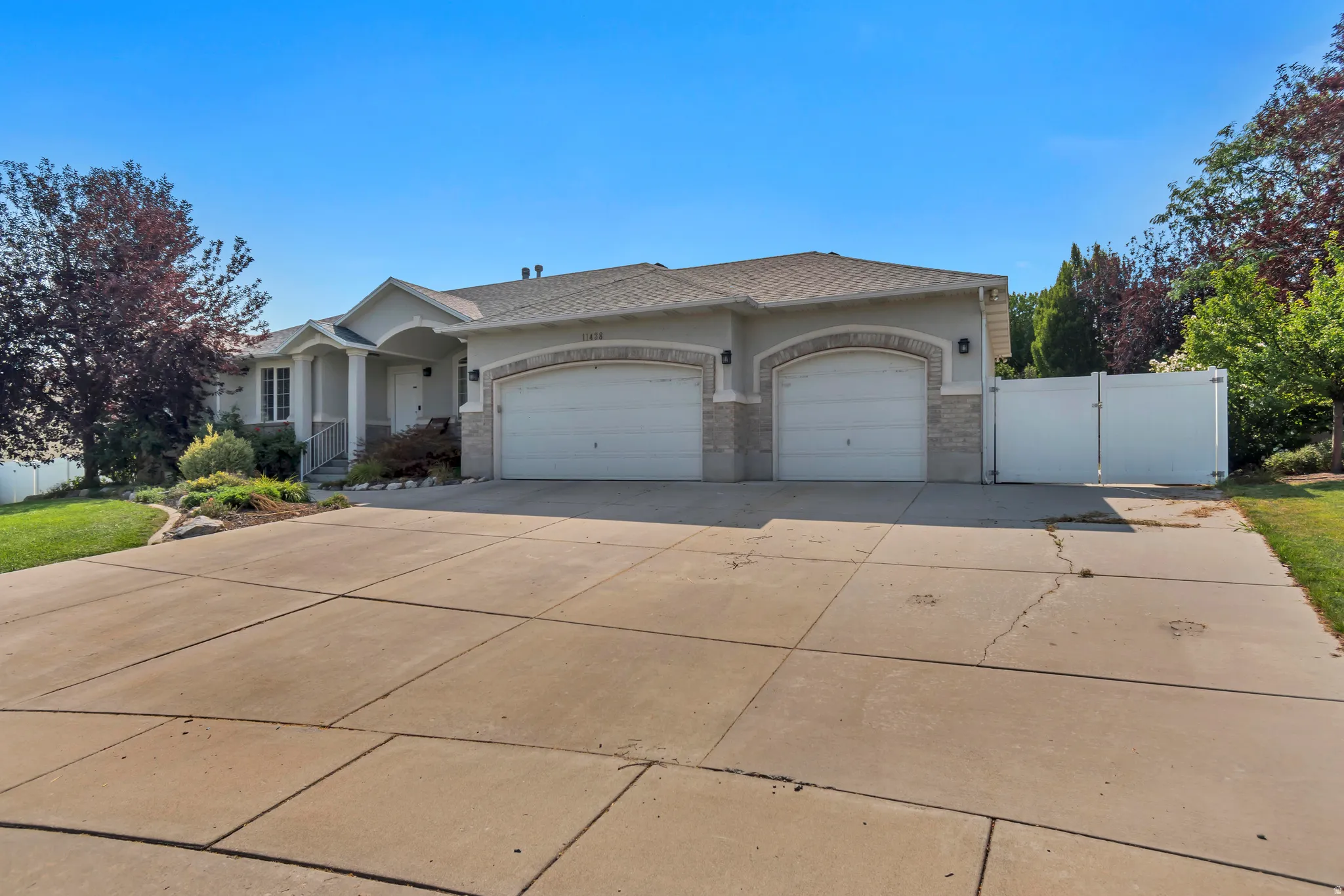 Welcoming ranch-style residence featuring a wide front elevation with dual two-car garage doors, arched architectural detailing, and stone accent work