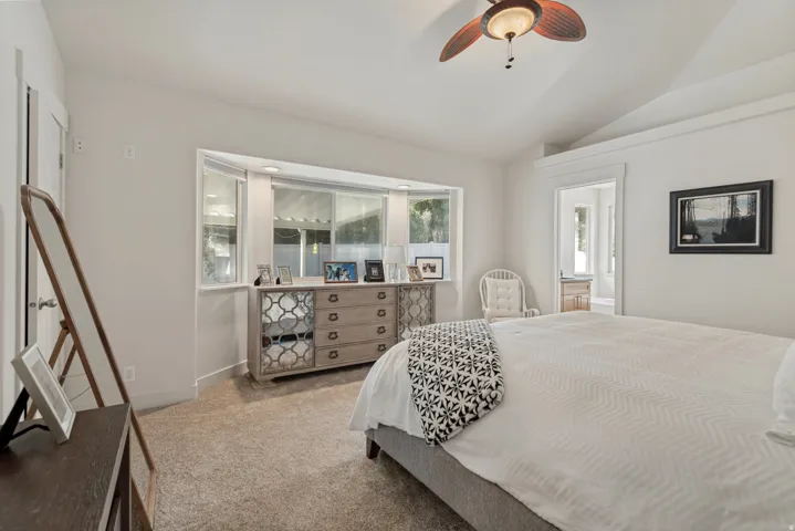 Bay window with sill, vaulted ceiling, ceiling fan, and carpeted flooring
