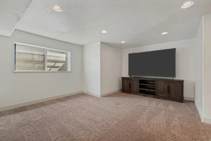 Spacious recreation room featuring plush carpeting, recessed ceiling lighting, and a custom wood-finish media console with integrated shelving