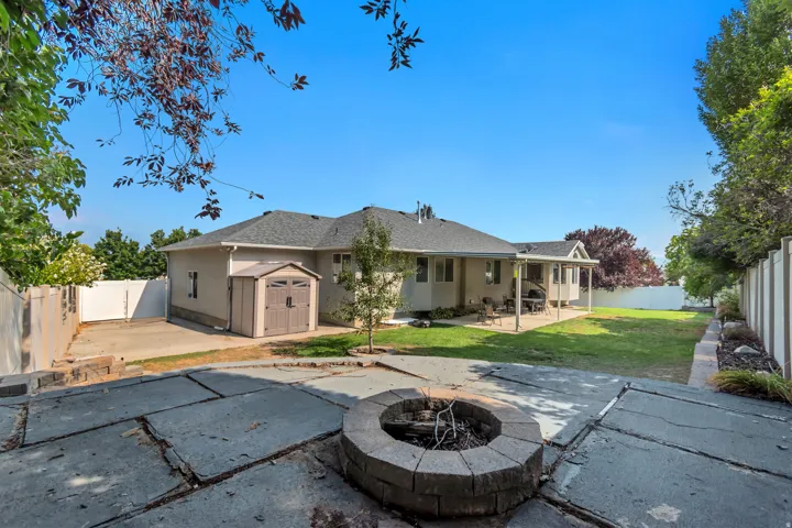 Expansive backyard oasis featuring a circular fire pit with stone surround, mature landscaping with established trees, manicured lawn, and generous hardscape patio space