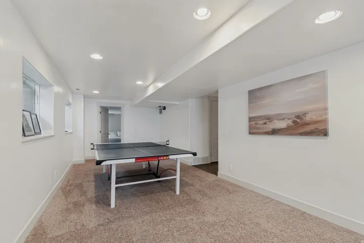 Finished recreation room featuring neutral carpet flooring, recessed lighting throughout the ceiling, and white walls with soft accent artwork