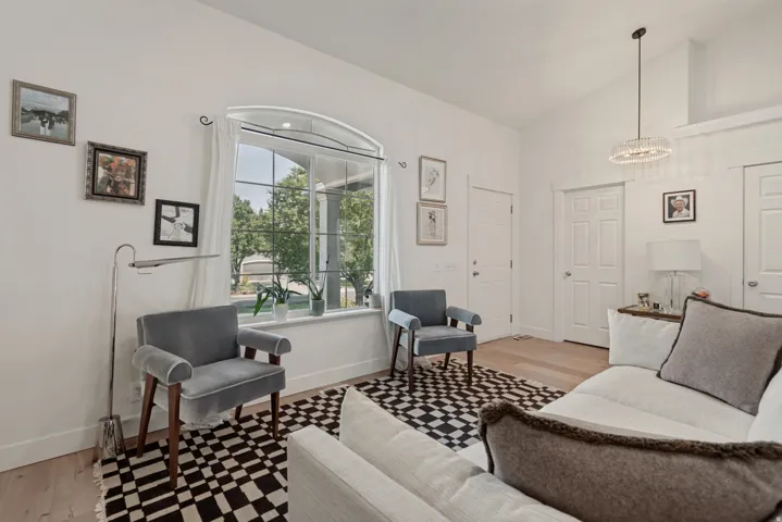 Bright bedroom featuring hardwood flooring, a large arched window with natural light, geometric patterned area rug, and white six-panel doors