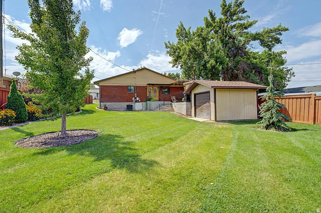 Expansive backyard featuring a manicured lawn, established trees, and a detached storage shed with an overhead door