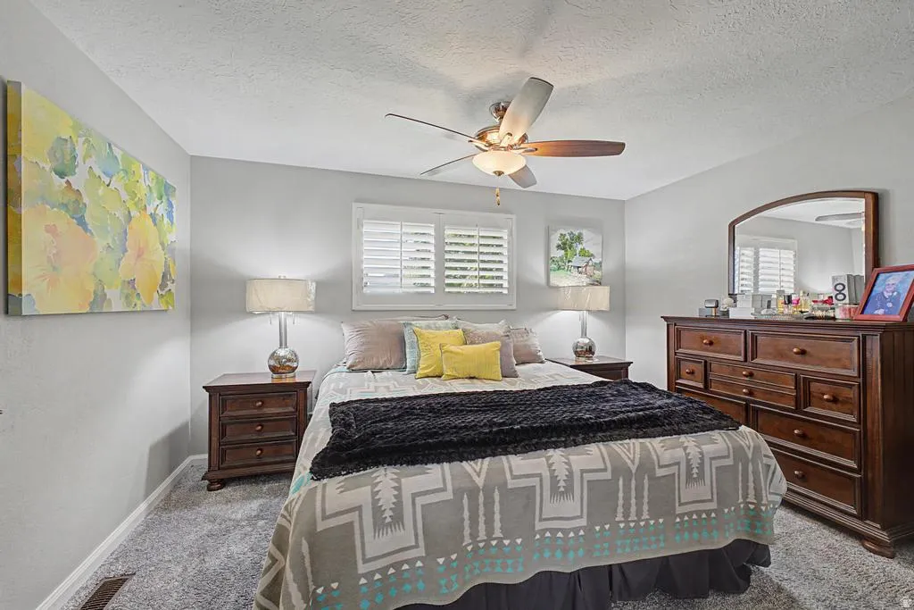 Ceiling fan with integrated lighting, window with white louvered shutters, light gray wall paint, and gray textured carpeting