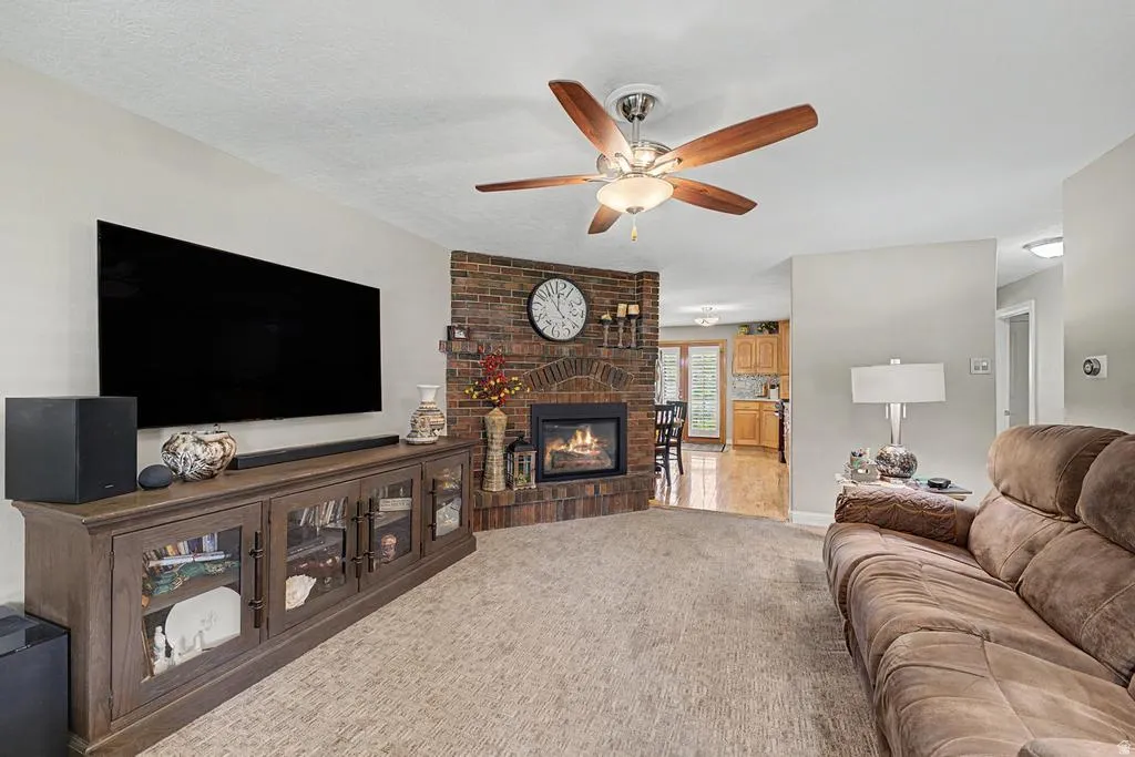 Brick fireplace, ceiling fan with light fixture, carpeted flooring, light-toned walls, and recessed lighting