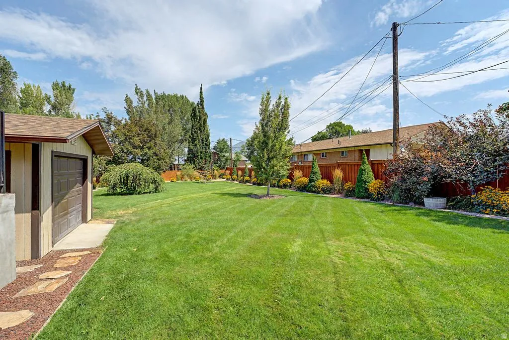 Expansive backyard featuring a lush, manicured lawn with mature landscaping including tall evergreens and flowering shrubs