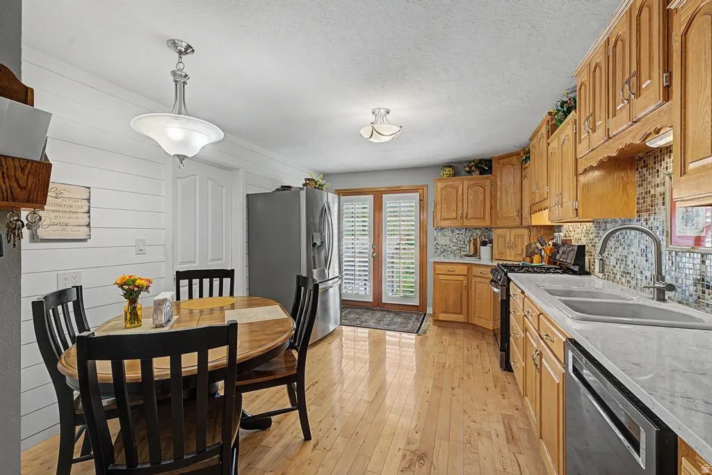 Kitchen featuring light wood-finish flooring, wood cabinetry, stainless steel appliances, and a mosaic tile backsplash