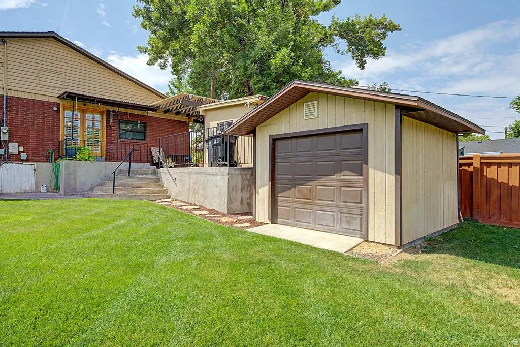 Expansive green lawn with a detached storage shed featuring a garage door, a concrete patio, and a brick exterior with a wood-finish siding upper level